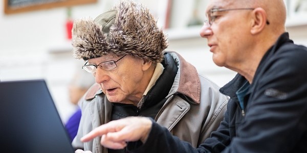 Two older adults looking at a computer, one pointing at the screen