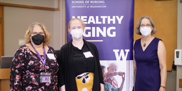 three people in masks stand in front of a healthy aging sign